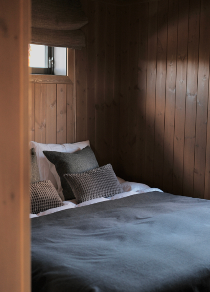 Bed filling the centre of a small room with wooden panels vertically positioned on the walls