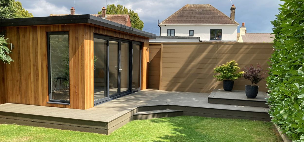 Outhouse in a garden with decking that surrounds it leading to the lawn.