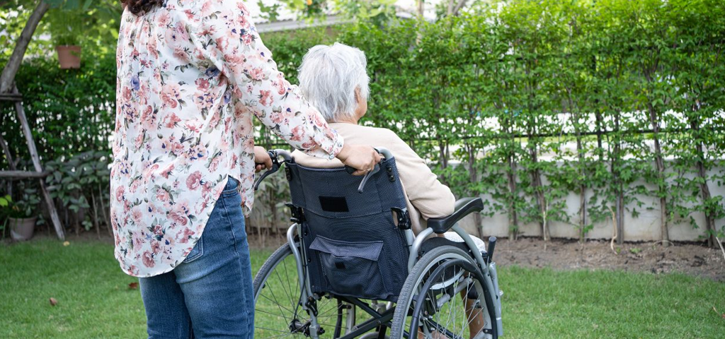 Woman pushing an elderly person in a wheelchair on grass.