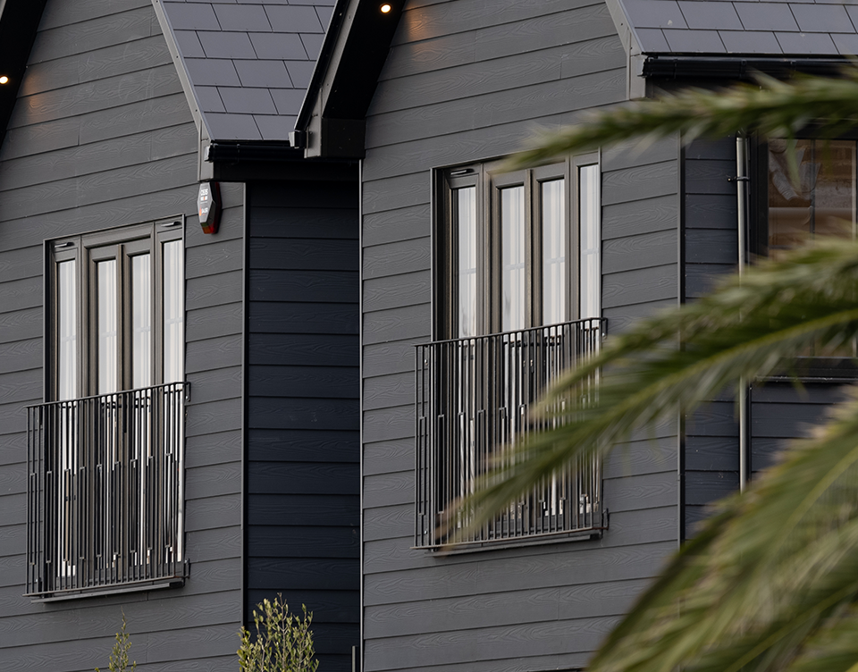 Enhanced view from the front of the house showing balcony and black fibre cement cladding.
